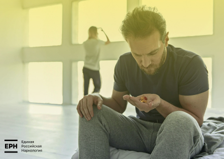 Мужчина сидит на кровати и смотрит на таблетки в руке